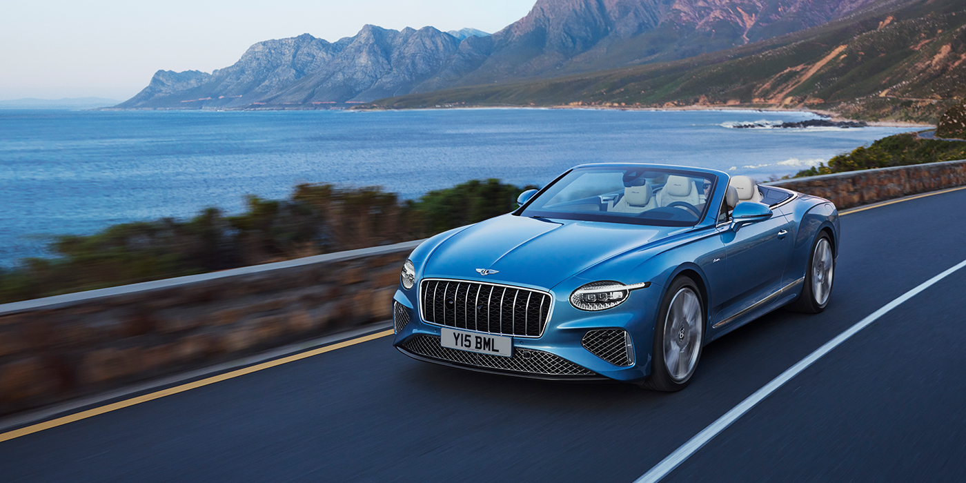 Bentley Berlin New Bentley Continental GTC Azure convertible in Light Windsor blue paint with 22 inch Azure wheels and chrome grill, driving dynamically by the sea