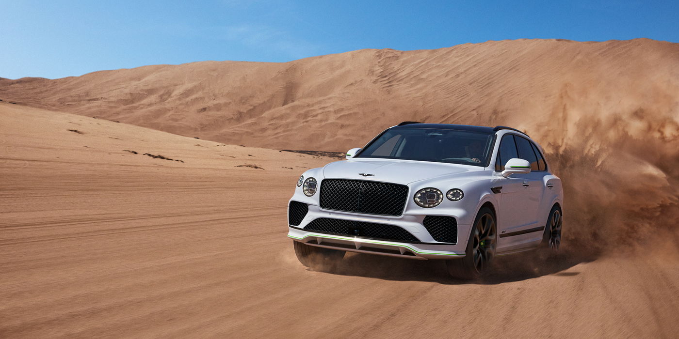 Bentley Berlin Bentley Bentayga Speed SUV front three quarter in Snow Quarts Pearlescent by Mulliner white paint driving dynamically through the desert
