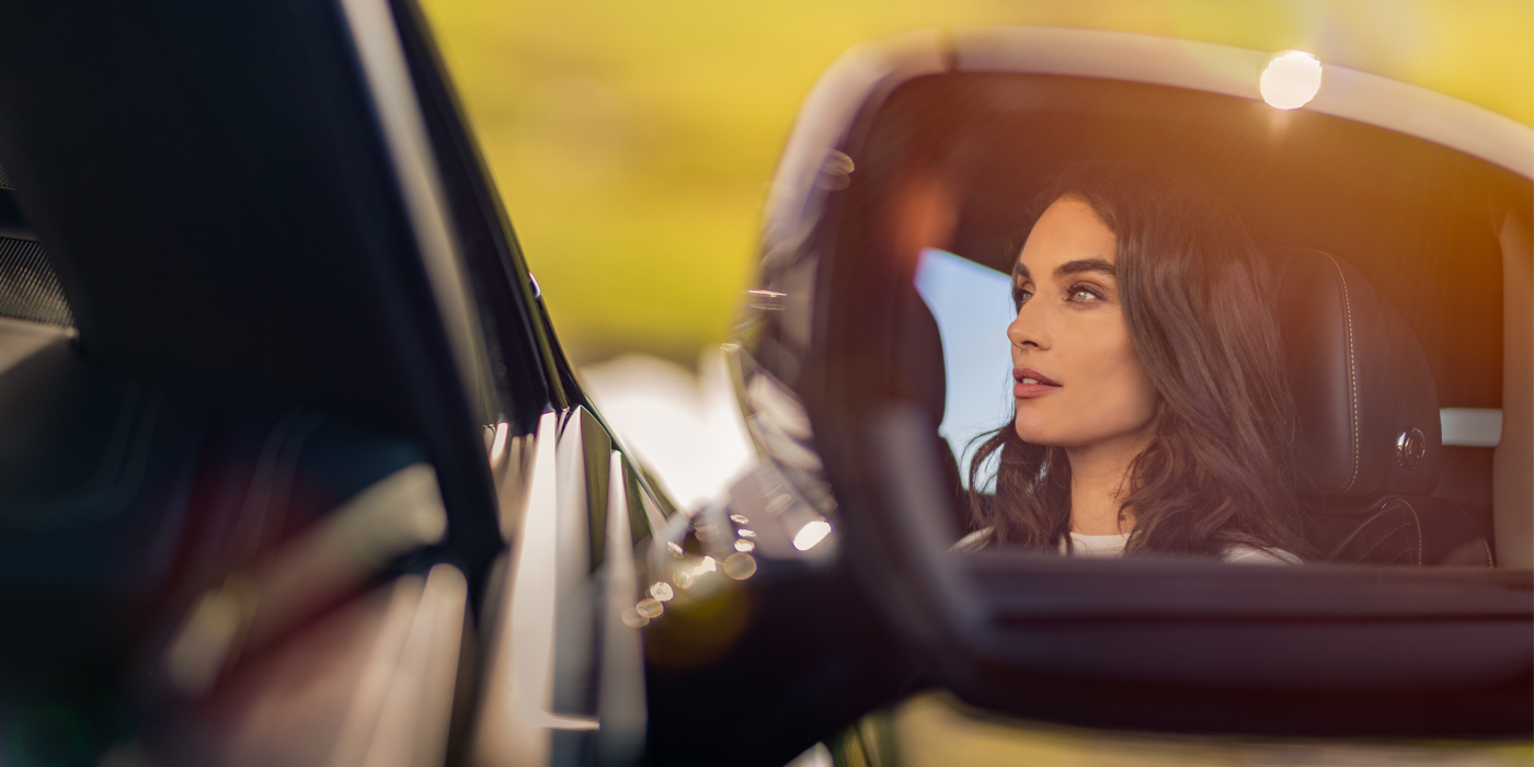Bentley Berlin profile of dark haired woman's face in mirror of Bentley car in sunlight