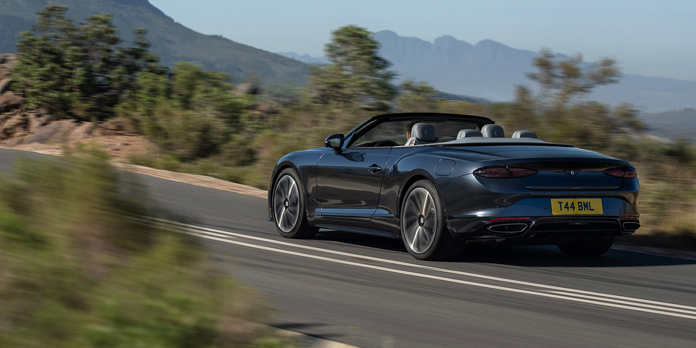 Bentley Berlin Bentley Continental GTC S convertible in Thunder blue paint rear 3/4 driving on mountain road