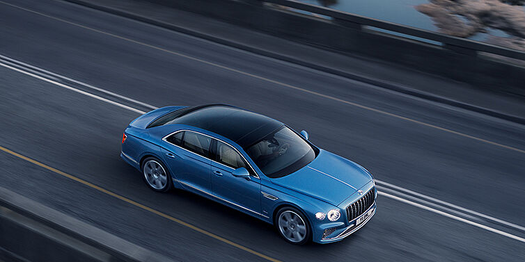 Bentley Berlin New Bentley Flying Spur Azure sedan in Light windsor blue paint by Mulliner, with 22 inch Azure wheels seen from overhead driving dynamically on a country road