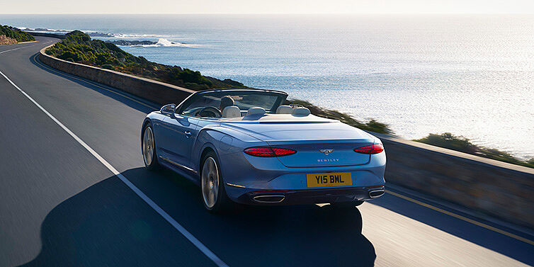 Bentley Berlin New Bentley Continental GTC Azure convertible rear view in Light Windsor blue paint with 22 inch ten spoke wheels driving dynamically on an ocean road in the sunshine