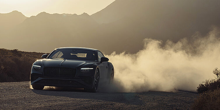 Bentley Berlin Bentley Continental GT Coupé in Thunder Lackierung vorne 3/4 bei Sonnenuntergang mit Staubwolke
