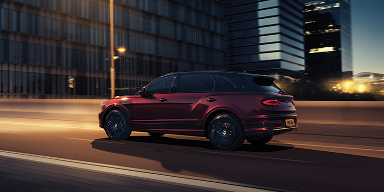 Bentley Berlin Bentley Bentayga Extended Wheelbase Mulliner SUV in Cricket Ball red paint driving dynamically in city at night